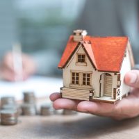 Man holding house and calculating estate plan with document and coins surrounding