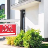 Red real estate sign near house outdoors on sunny day