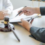 Lawyer hand holding pen and providing legal consult business dispute service at the office with justice scale and gavel hammer.