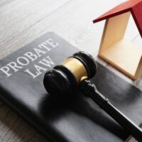 Gavel on a "Probate Law" book beside a wooden house model with a red roof. Represents legal aspects of estate and property management.
